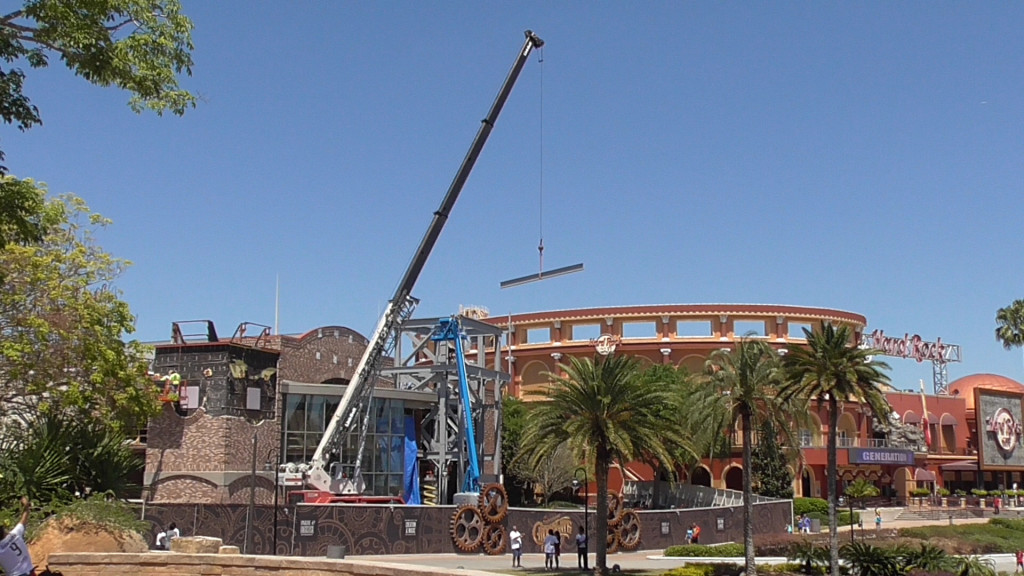 Crane lifting steel beam into place, as the facade grows