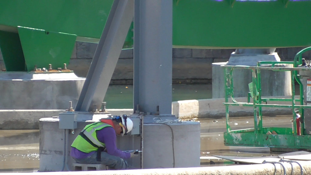 Workers installing electrical boxes at base of supports