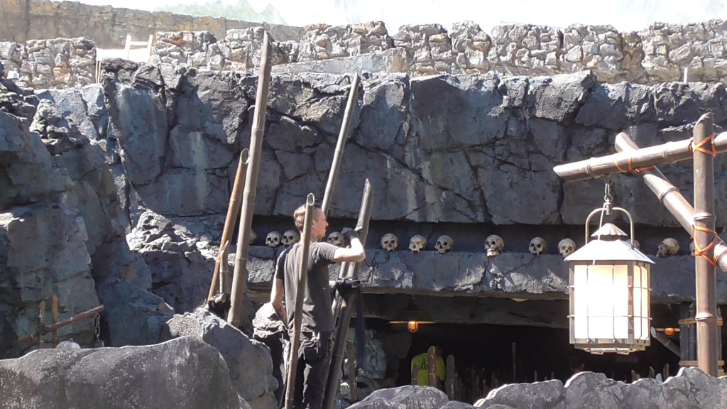 Crew member weather-proofing/painting bamboo stakes amidst a wall of skulls